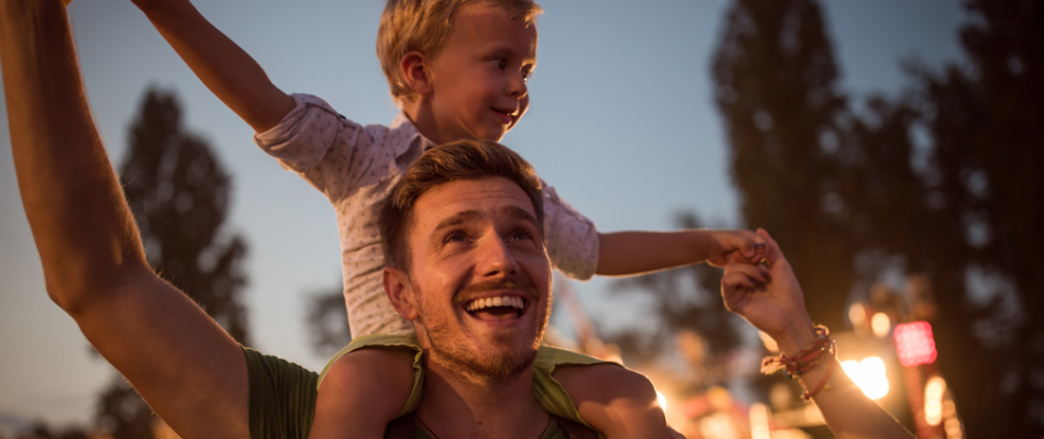 man with toddler on shoulders at a festival
