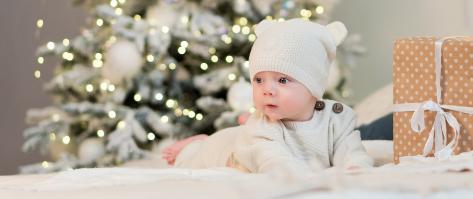 baby in white in front of a christmas tree