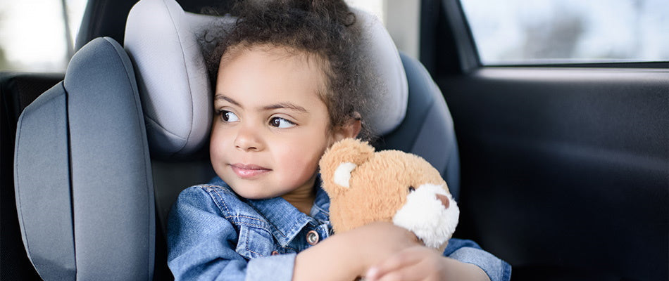 girl in car seat holding teddy